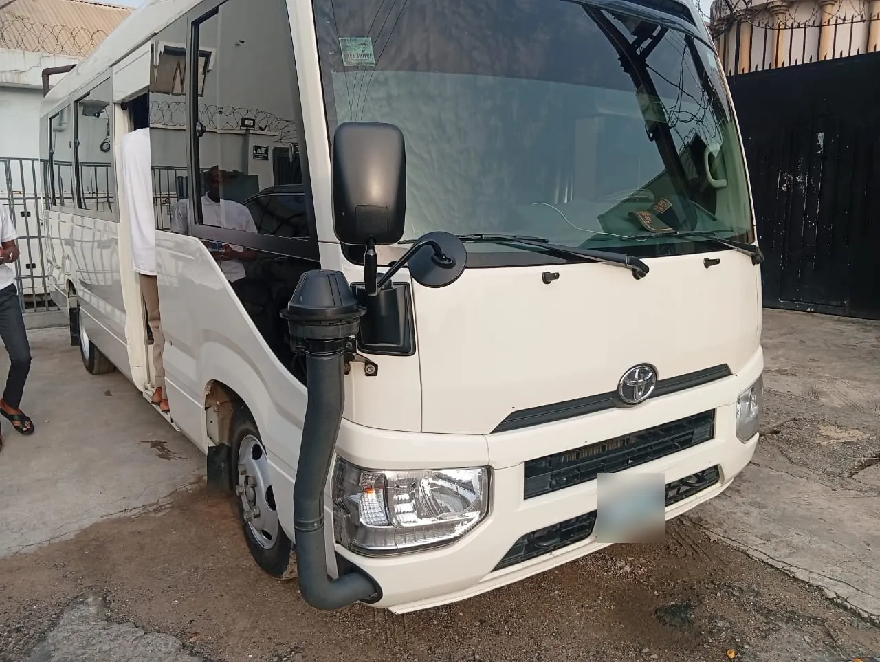White Toyota Coaster bus, front left angle view with the passenger door open
