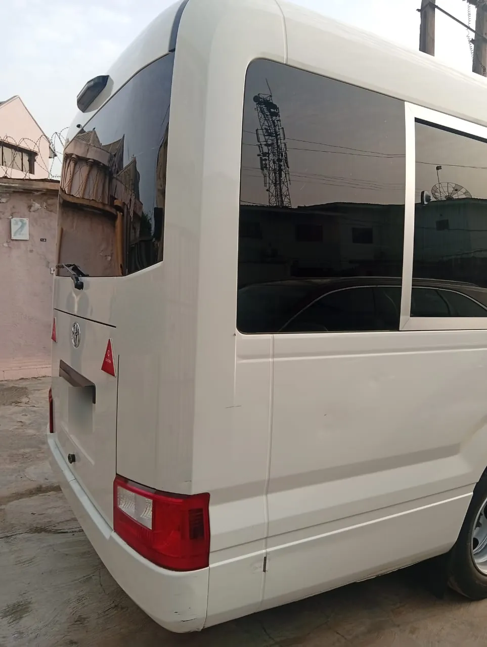 Rear corner of a white Toyota Coaster bus showing the tail light and rear windows